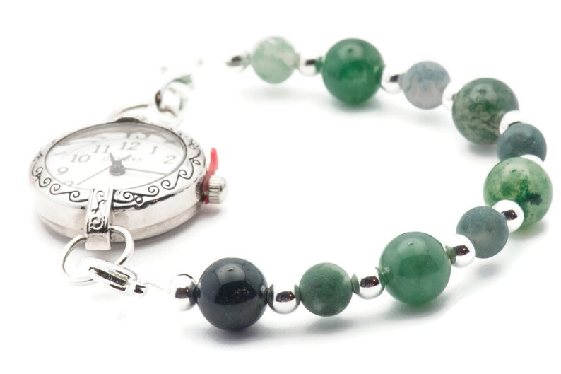 May include: A silver pocket watch with a white face and black hands is attached to a bracelet made of green and grey beads.