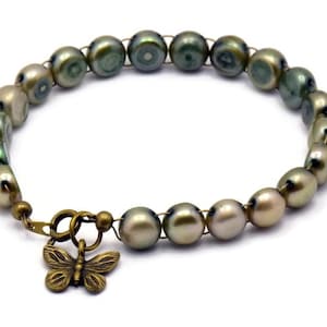 Op de afbeelding: Een groene en gouden parel armband met een bronzen vlinder bedel. De armband is gemaakt van draad en parels.