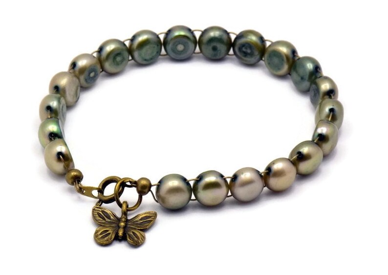 Op de afbeelding: Een groene en gouden parel armband met een bronzen vlinder bedel. De armband is gemaakt van draad en parels.