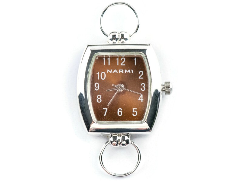 Puede incluir: Un reloj plateado con una esfera marr&oacute;n y forma cuadrada. El reloj tiene un bucle en la parte superior e inferior para sujetarlo a una cadena o pulsera. La esfera del reloj tiene la palabra "NARMI" impresa.