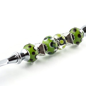May include: A silver letter opener with a green, black and white patterned glass bead handle.