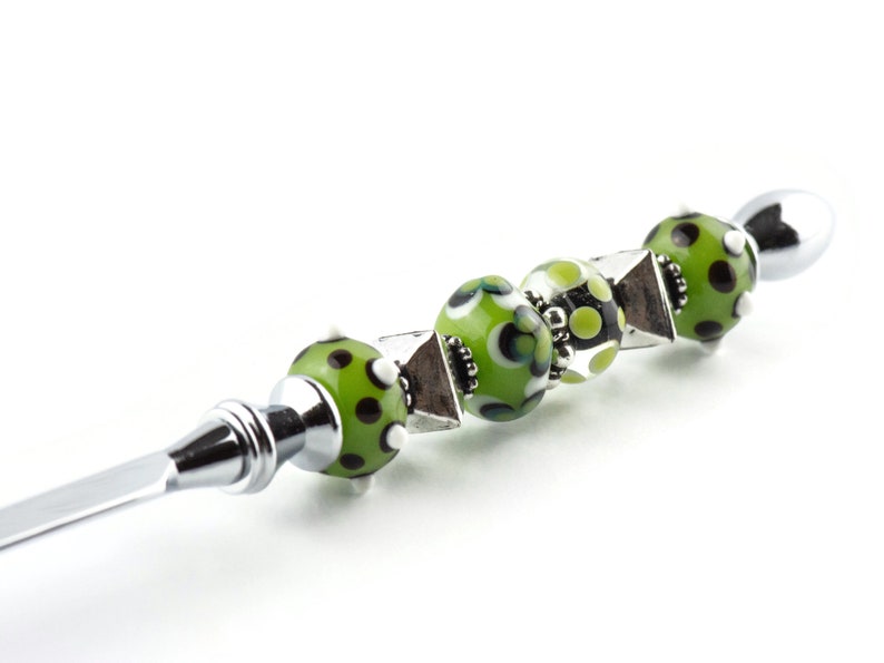 May include: A silver letter opener with a green, black and white patterned glass bead handle.