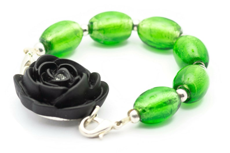 May include: A black rose charm bracelet with green glass beads. The bracelet has a silver clasp.