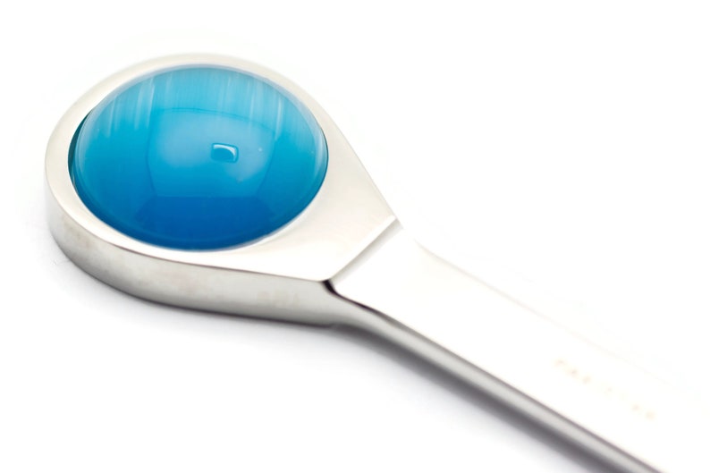 K&ouml;nnte beinhalten: Nahaufnahme eines silberfarbenen Werkzeugs mit einem blauen, runden, glasartigen Kopf.