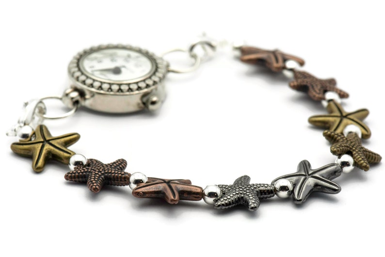 May include: A silver watch with a white face and black hands is attached to a bracelet with silver and bronze starfish charms.