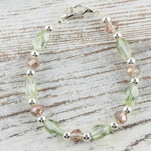May include: A silver bracelet with green and pink glass beads. The bracelet has a silver clasp.
