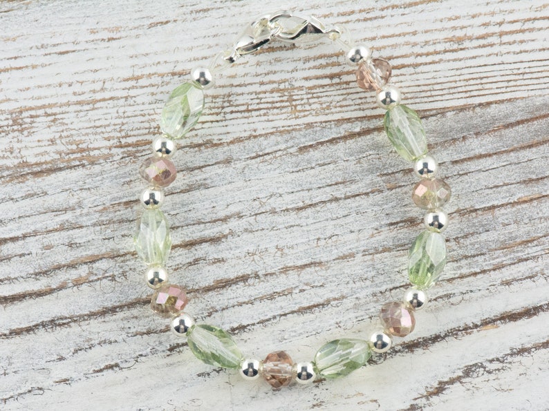 May include: A silver bracelet with green and pink glass beads. The bracelet has a silver clasp.