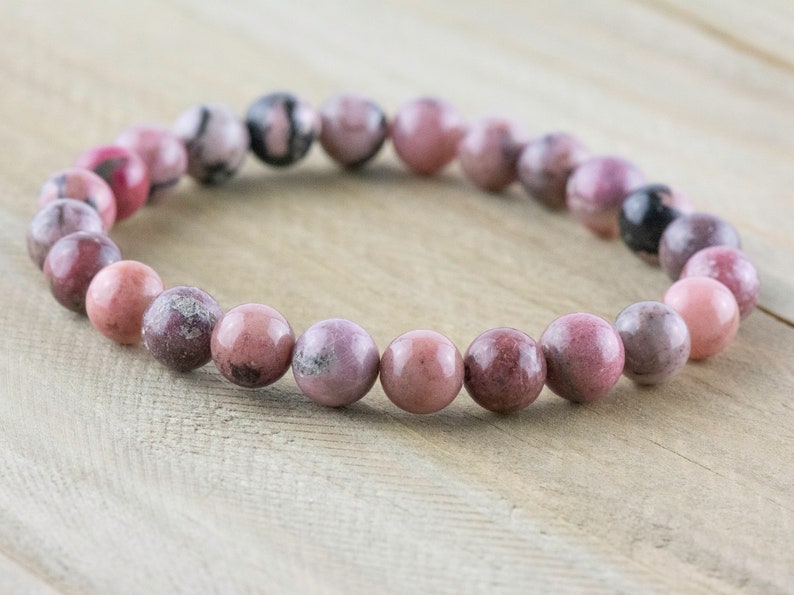 May include: A pink and gray gemstone bracelet with round beads. The bracelet is made of natural stones and is approximately 7 inches in length.