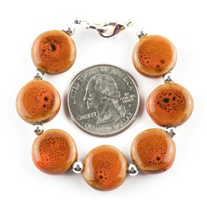 May include: A bracelet made of round, orange ceramic beads with a silver clasp. The beads are about the size of a US quarter.