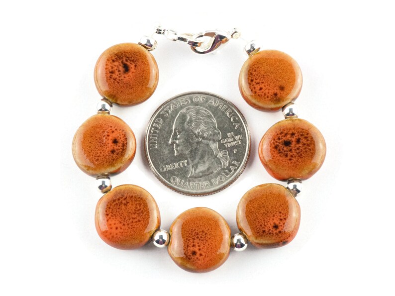 May include: A bracelet made of round, orange ceramic beads with a silver clasp. The beads are about the size of a US quarter.