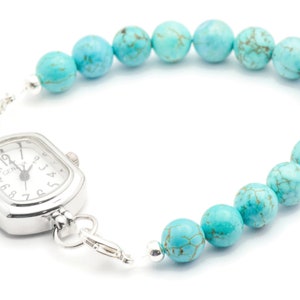 May include: A silver watch with a square face and turquoise beads attached to the band. The watch face has black Roman numeral markings and a silver second hand.
