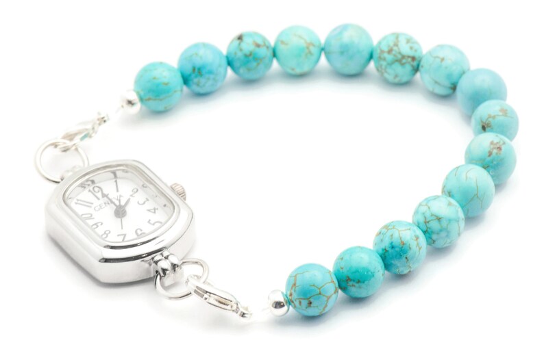 May include: A silver watch with a square face and turquoise beads attached to the band. The watch face has black Roman numeral markings and a silver second hand.