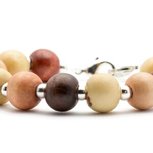 Puede incluir: Un brazalete de cuentas de madera con cierre de plata. Las cuentas son en tonos de marr&oacute;n, beige y rojo.