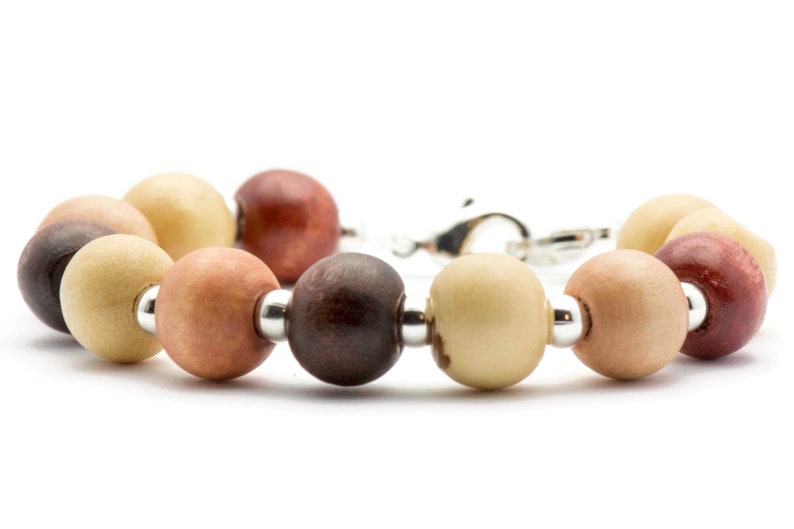 Puede incluir: Un brazalete de cuentas de madera con cierre de plata. Las cuentas son en tonos de marr&oacute;n, beige y rojo.