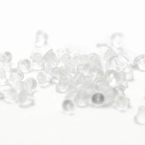 May include: A pile of clear plastic earring backs. The backs are small and round, with a slight lip around the edge.