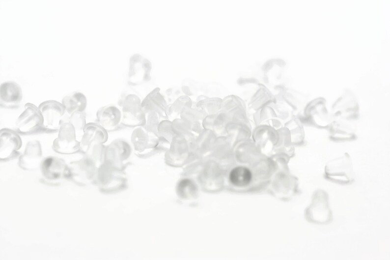 May include: A pile of clear plastic earring backs. The backs are small and round, with a slight lip around the edge.