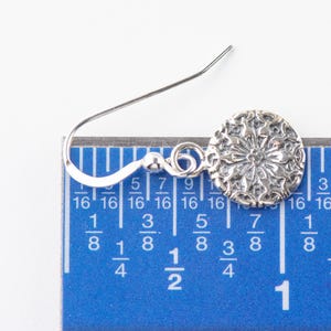 May include: Silver dangle earring with a circular floral design. The earring is measured against a ruler, showing it is about 7/8 inch long.