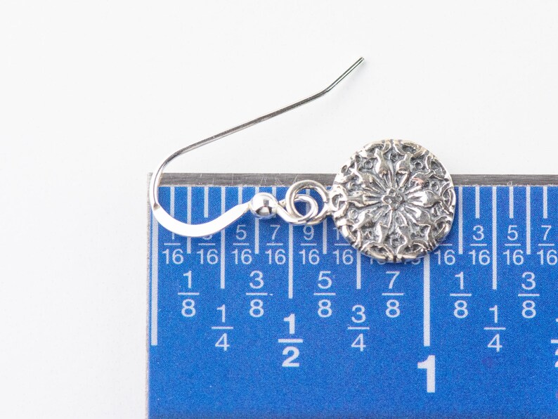 May include: Silver dangle earring with a circular floral design. The earring is measured against a ruler, showing it is about 7/8 inch long.