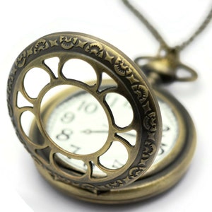 K&ouml;nnte beinhalten: Eine goldfarbene Taschenuhr mit einem verzierten, offenen Design. Die Uhr hat ein wei&szlig;es Zifferblatt mit schwarzen r&ouml;mischen Ziffern f&uuml;r die Stunden und schwarzen Zeigern.