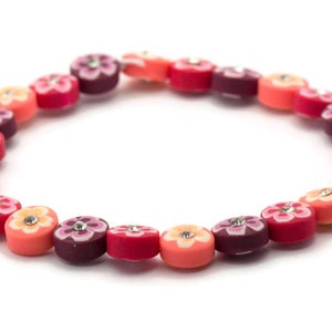 K&ouml;nnte beinhalten: Ein farbenfrohes Armband aus runden Perlen mit Blumendesigns und Strasssteinen. Die Perlen sind in den Farben Rosa, Orange und Lila.
