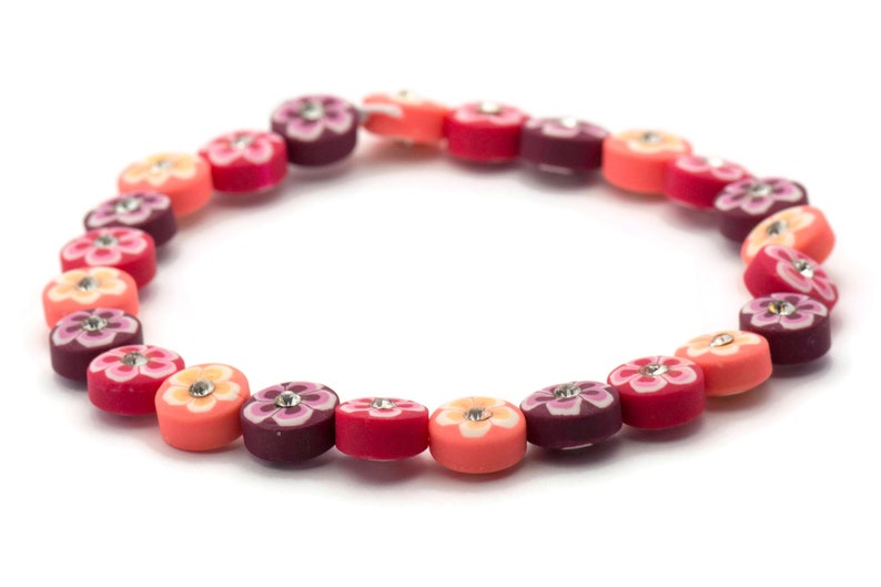 K&ouml;nnte beinhalten: Ein farbenfrohes Armband aus runden Perlen mit Blumendesigns und Strasssteinen. Die Perlen sind in den Farben Rosa, Orange und Lila.