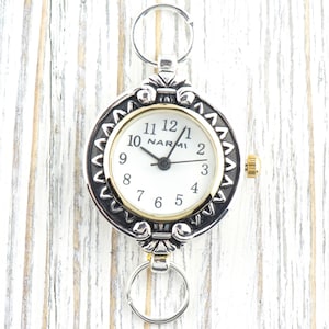 Pu&ograve; includere: Orologio da tasca color argento con quadrante bianco e dettagli dorati. L'orologio presenta il marchio "NARMI" e una lunetta decorativa. Include portachiavi nella parte superiore e inferiore per il fissaggio.