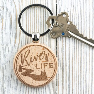 May include: A wooden keyring with a silver key ring. The keyring is round and has the words "River Life" engraved on it. There is a small image of a river and trees engraved on the keyring.