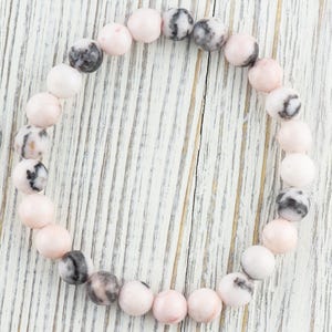 May include: A pink and black gemstone bracelet with round beads. The bracelet is made of natural stones and is a beautiful accessory for any occasion.