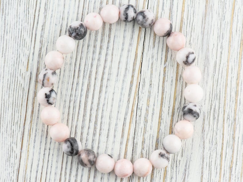 May include: A pink and black gemstone bracelet with round beads. The bracelet is made of natural stones and is a beautiful accessory for any occasion.