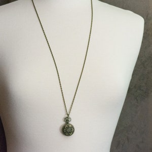 May include: A bronze chain necklace with a round pendant featuring a floral design.