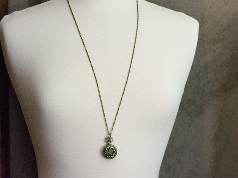 May include: A bronze chain necklace with a round pendant featuring a floral design.