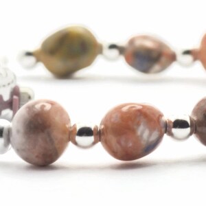 May include: A silver watch with a white face and a brown and white beaded bracelet.