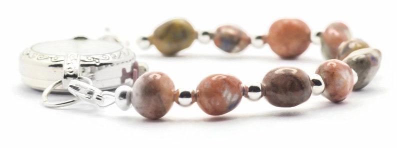 May include: A silver watch with a white face and a brown and white beaded bracelet.