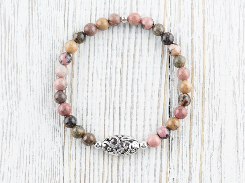 Puede incluir: Un brazalete de piedras preciosas rosa, marr&oacute;n y gris con un dije de plata. El brazalete est&aacute; hecho de cuentas redondas y tiene un cierre de plata.