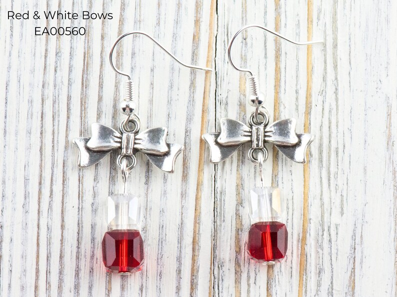 Pode incluir: Brincos de la&ccedil;o prateados com uma gota de joia transparente e vermelha. Os brincos t&ecirc;m fecho de gancho. O texto "Red & White Bows" e "EA00560" est&aacute; no canto superior esquerdo.