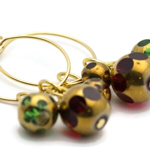 May include: Gold hoop earrings with three dangling beads. The beads are gold with red and green polka dots.