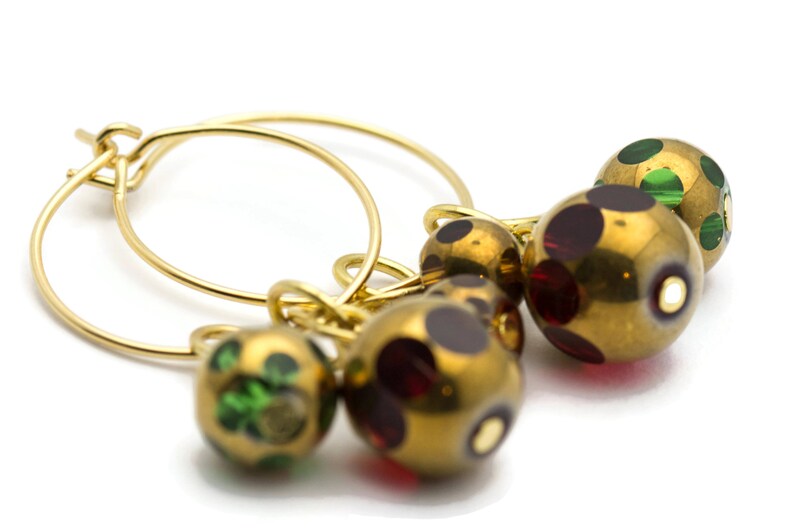 May include: Gold hoop earrings with three dangling beads. The beads are gold with red and green polka dots.
