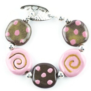 May include: A bracelet with brown and pink ceramic beads. The beads have different patterns, including polka dots and swirls. The bracelet has a silver clasp.