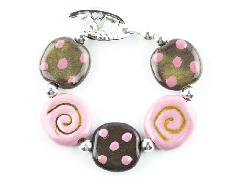 May include: A bracelet with brown and pink ceramic beads. The beads have different patterns, including polka dots and swirls. The bracelet has a silver clasp.