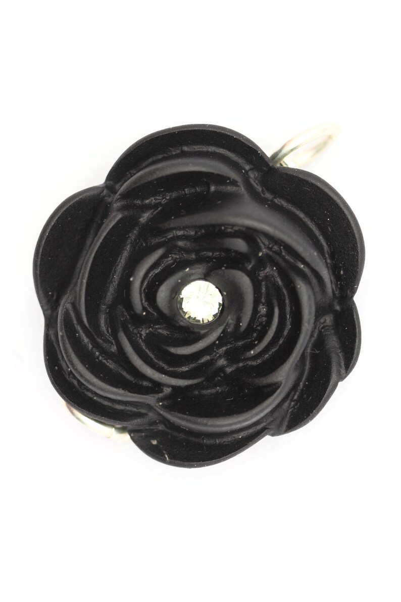 May include: A black rose-shaped charm with a clear rhinestone in the center. The charm has a silver loop for attaching to a necklace or bracelet.