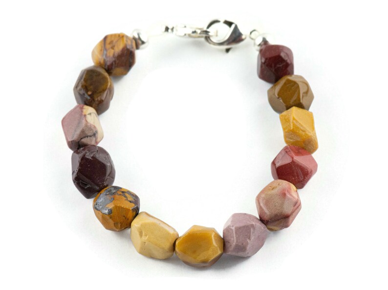 May include: A multi-colored gemstone bracelet with a silver clasp. The bracelet features a variety of colors, including red, brown, and yellow.