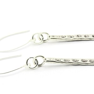 May include: A pair of silver dangle earrings with a textured bar design. The bar has a repeating pattern of small circles.