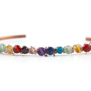 K&ouml;nnte beinhalten: Ein mit Kupferdraht umwickeltes Armband mit einem Regenbogen aus Edelsteinen, darunter Amethyst, Lapislazuli, T&uuml;rkis und klarer Quarz.