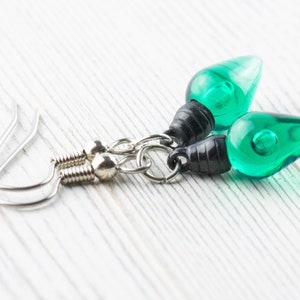 Op de afbeelding: Een paar groene lampenbolvormige oorbellen met zwarte accenten en zilveren haakjes.
