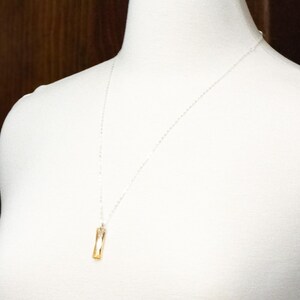 May include: A silver chain necklace with a gold rectangular pendant.