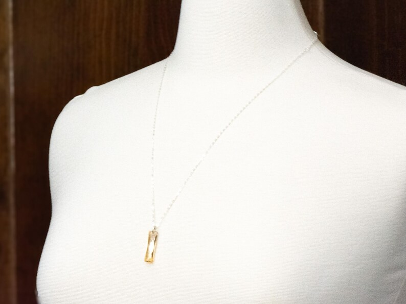 May include: A silver chain necklace with a gold rectangular pendant.