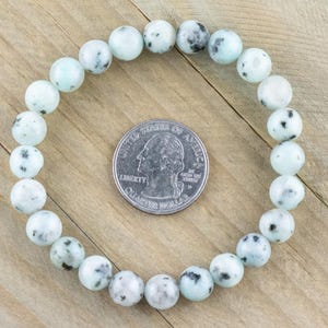 Puede incluir: Un brazalete hecho de cuentas de color azul claro y blanco con motas. El brazalete es del tama&ntilde;o de una moneda de 25 centavos.