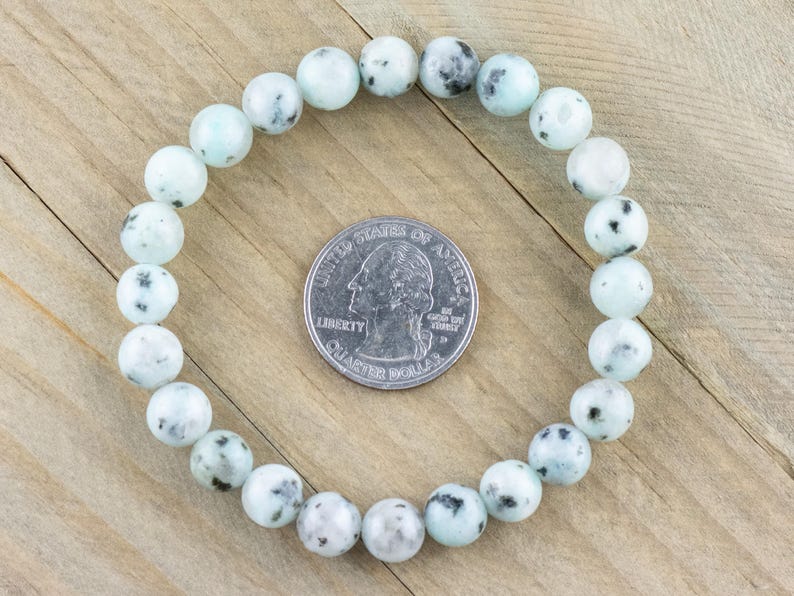 Puede incluir: Un brazalete hecho de cuentas de color azul claro y blanco con motas. El brazalete es del tama&ntilde;o de una moneda de 25 centavos.