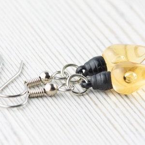 Op de afbeelding: Een paar oorhangers met amberkleurige, traanvormige glazen kralen en zwarte accenten. De oorhangers hebben zilveren haakjes.