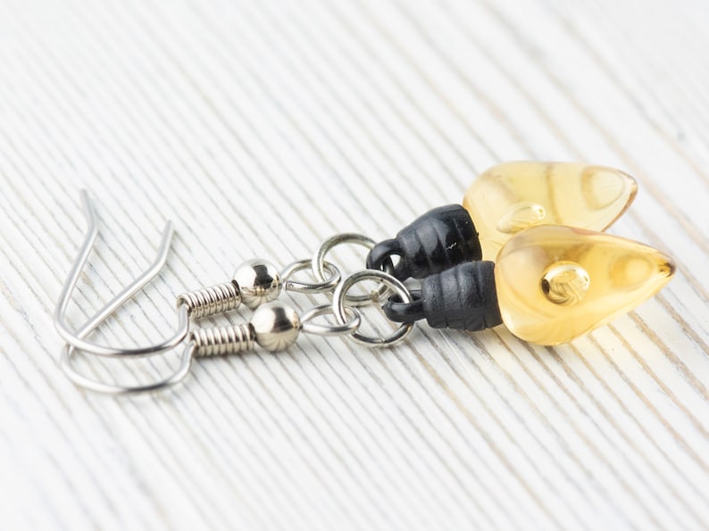 Op de afbeelding: Een paar oorhangers met amberkleurige, traanvormige glazen kralen en zwarte accenten. De oorhangers hebben zilveren haakjes.